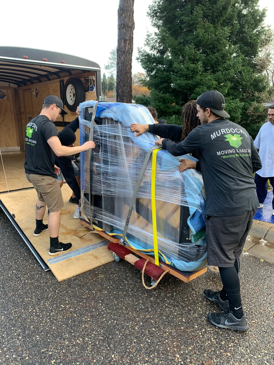 Murdock's Moving & Storage crew in branded shirts wrapping and loading a piano onto a moving trailer
