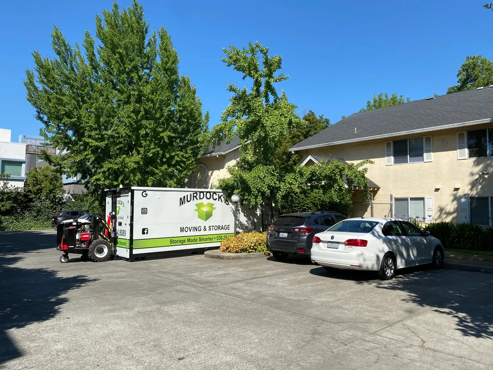 Murdock's Moving & Storage MODS container being positioned by a compact forklift in an apartment driveway