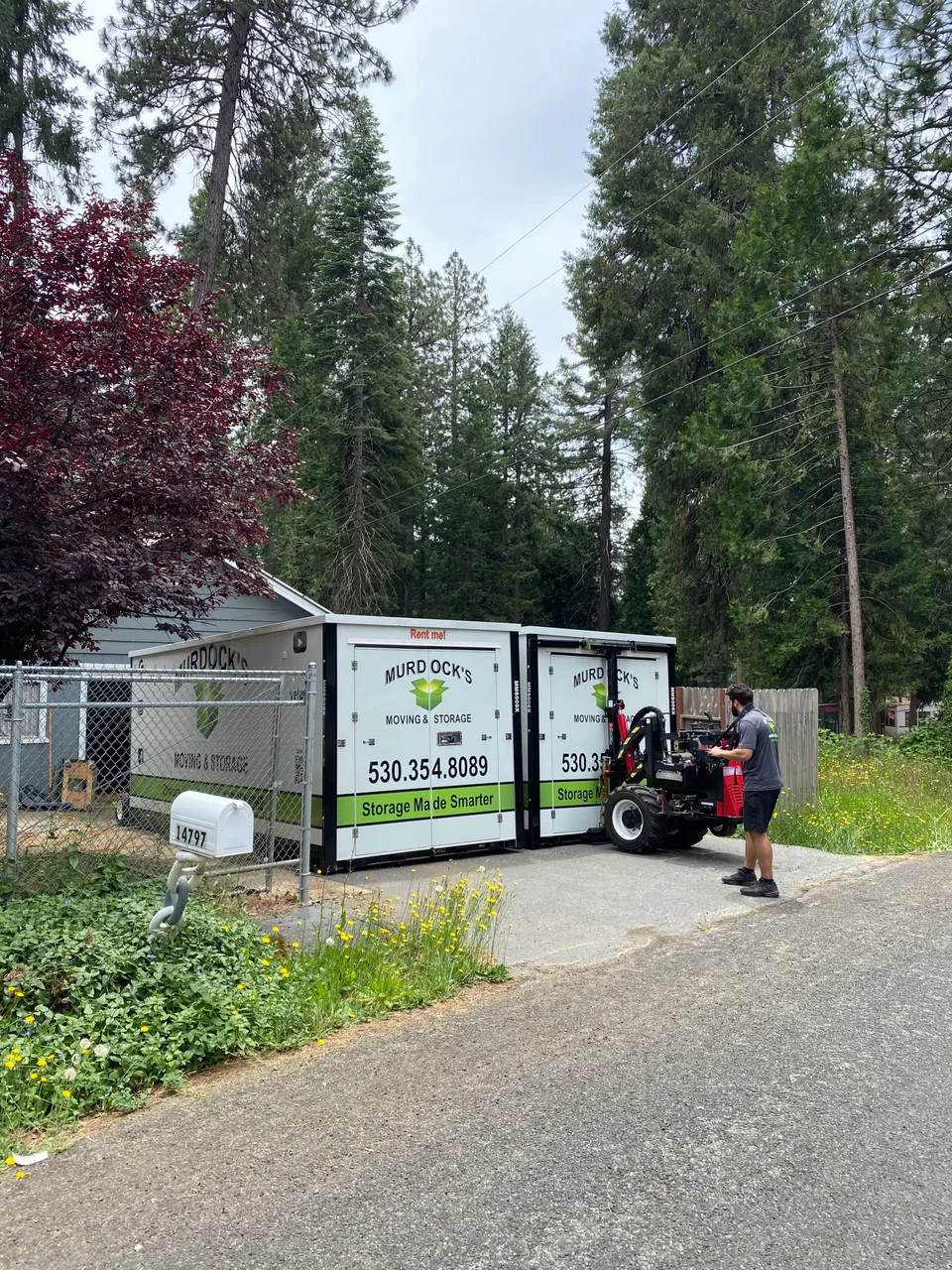 Two Murdock's Moving & Storage MODS containers with a crew member operating a power mover in a residential yard