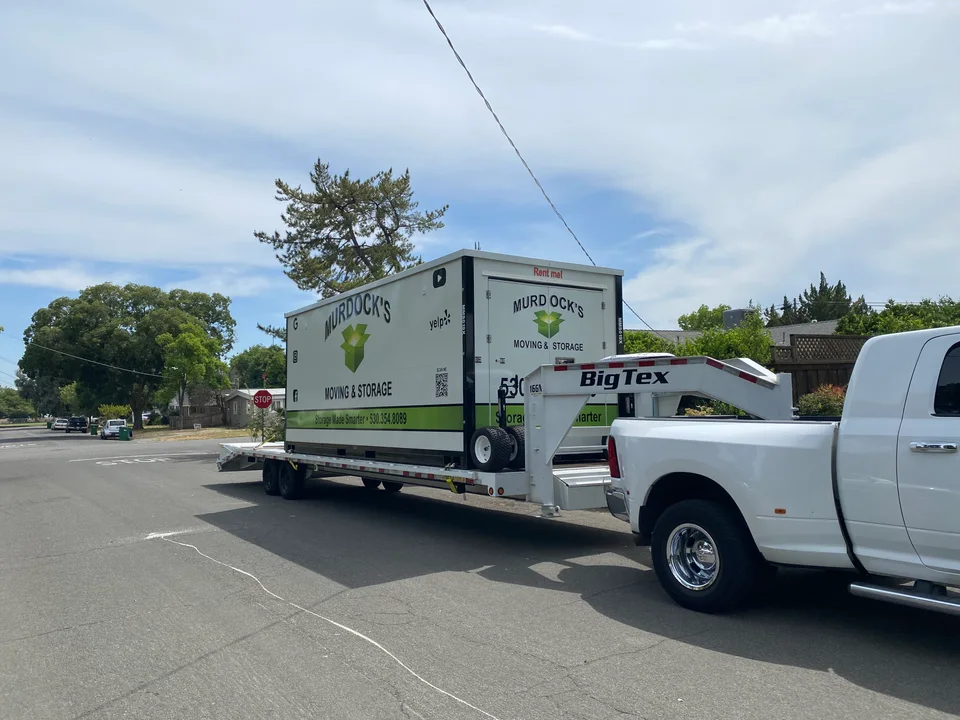 Murdock's Moving & Storage MODS container loaded on a Big Tex gooseneck trailer towed by a white dually truck