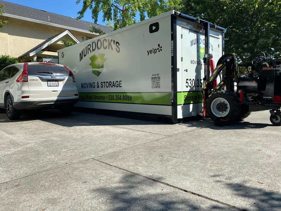 Murdock's Moving & Storage MODS container maneuvered by a Mule power mover next to a parked Honda in a driveway