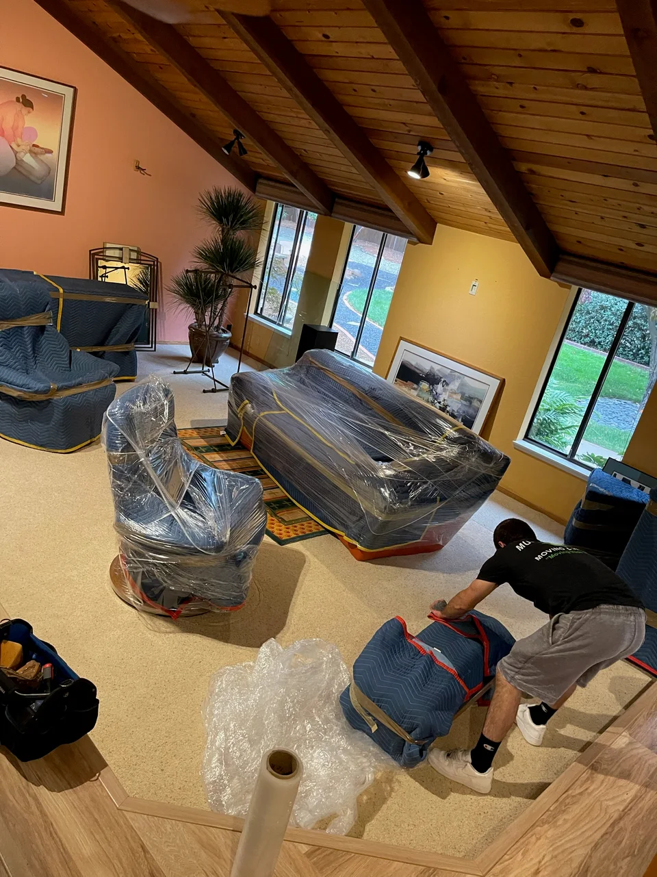 Murdock's Moving & Storage mover shrink-wraps and blanket-pads sofas and chairs in a living room being packed