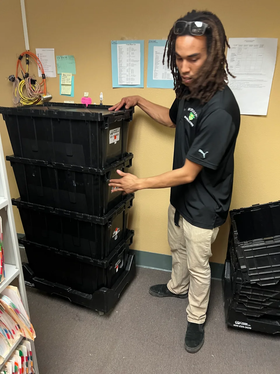 Murdock's Moving & Storage crew member stands beside stacked black plastic moving totes in an office
