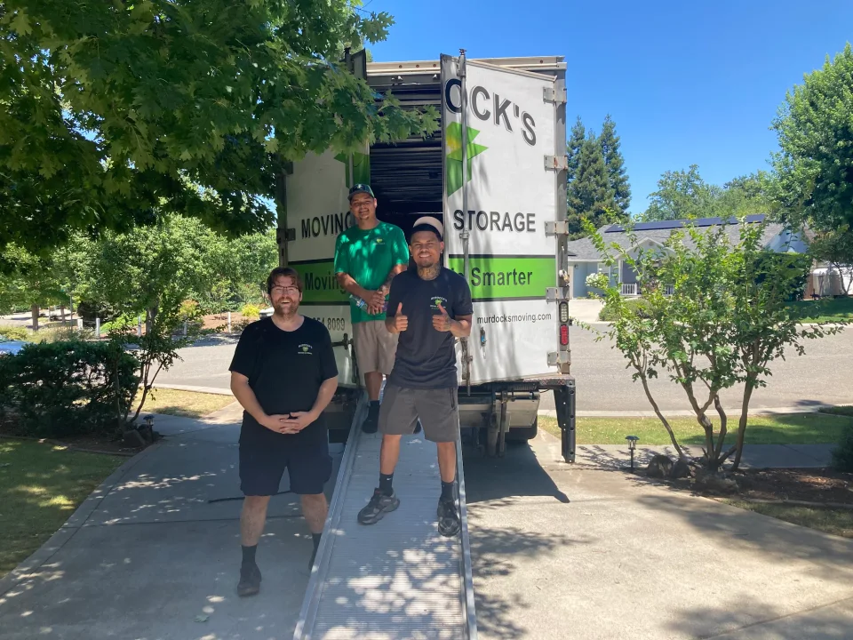 Three Murdock's Moving crew members on the loading ramp of an open box truck in a residential driveway