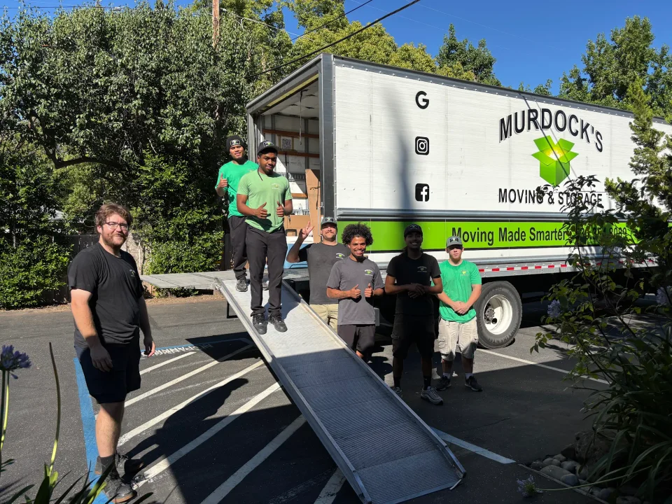 Group of Murdock's Moving & Storage crew members posing at the truck's loading ramp giving thumbs up