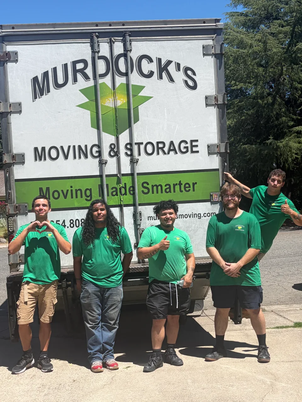 Five Murdock's Moving & Storage crew members in green shirts pose at the rear of the branded moving truck