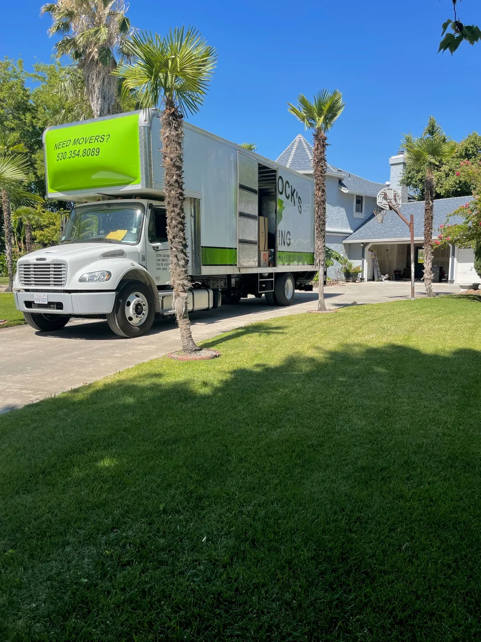 Green and white Murdock's Moving & Storage box truck parked in a sunny driveway lined with palm trees